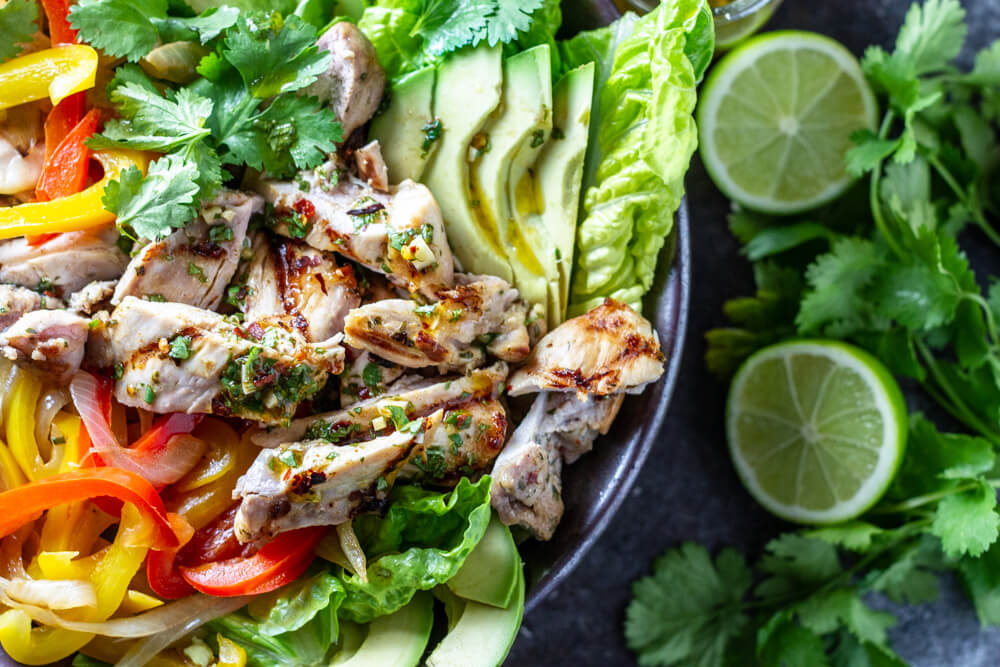 Chicken Fajita Salad in black bowl with limes and avocado