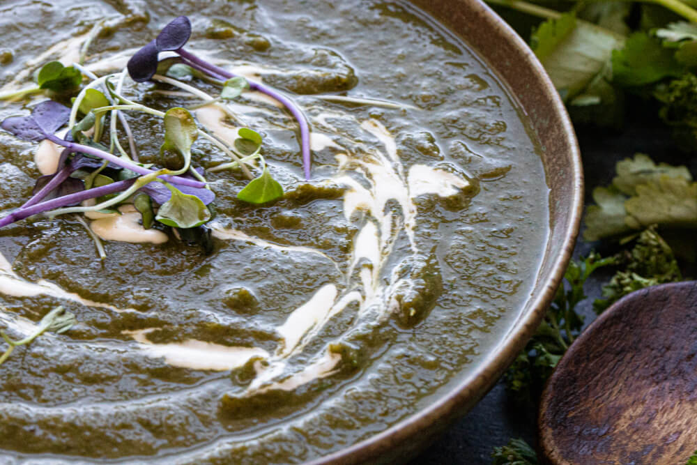 green soup in green bowl with cream on top