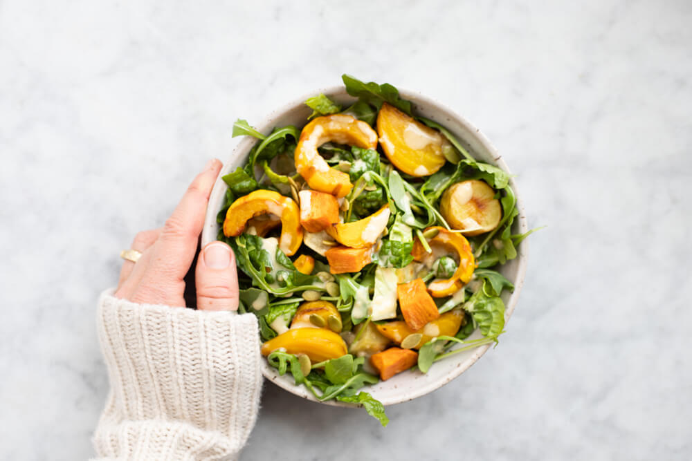 hand holding white bowl with winter salad