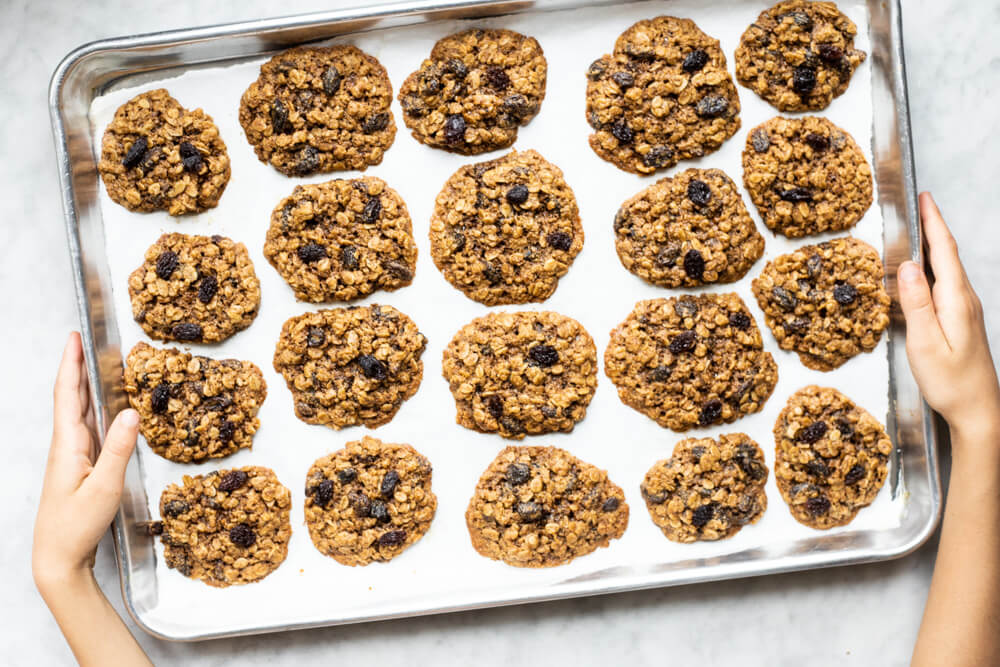 hands holding silver tray of gluten free oatmeal raisin cookies