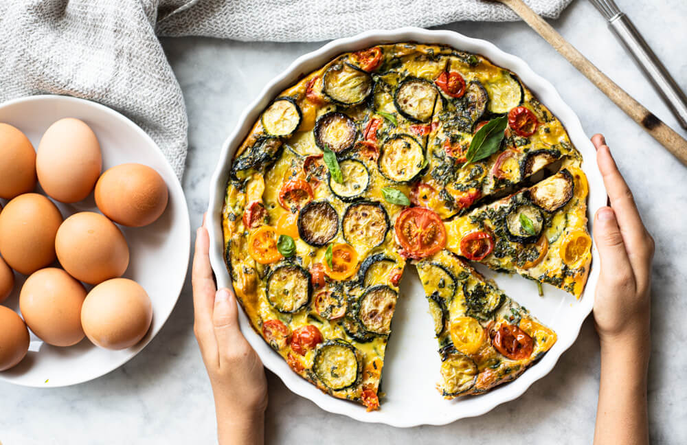 hands holding white dish with crustless quiche