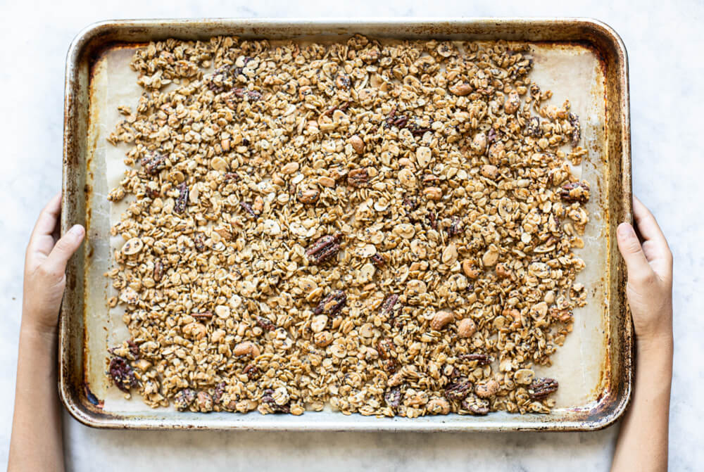 hands holding baking tray of granola