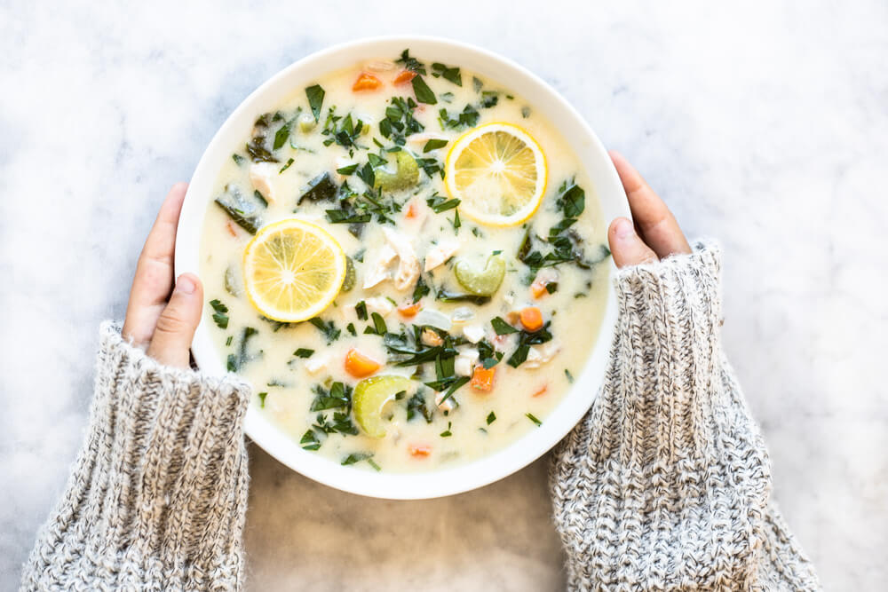 hands holding white bowl of soup