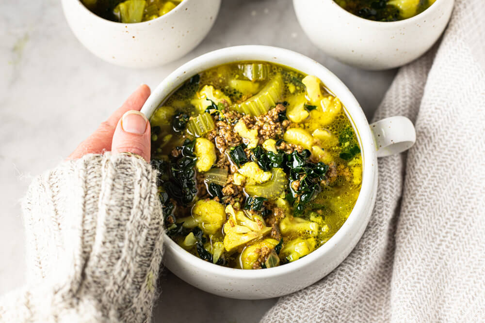 hand holding white bowl of soup
