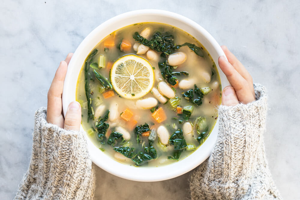 hands holding white bowl of soup