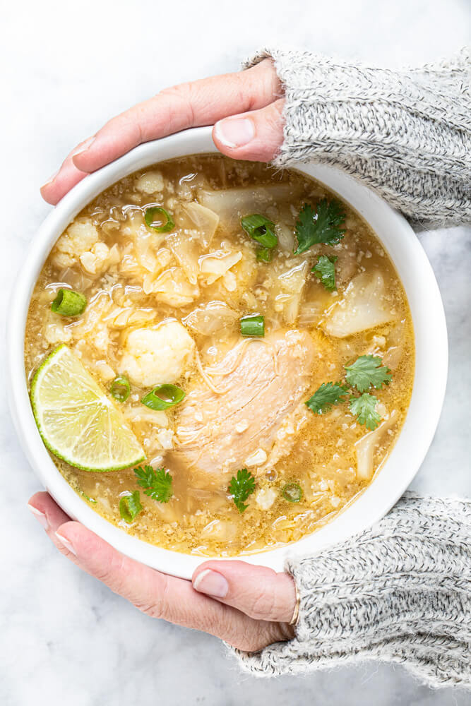 hands holding white bowl with soup
