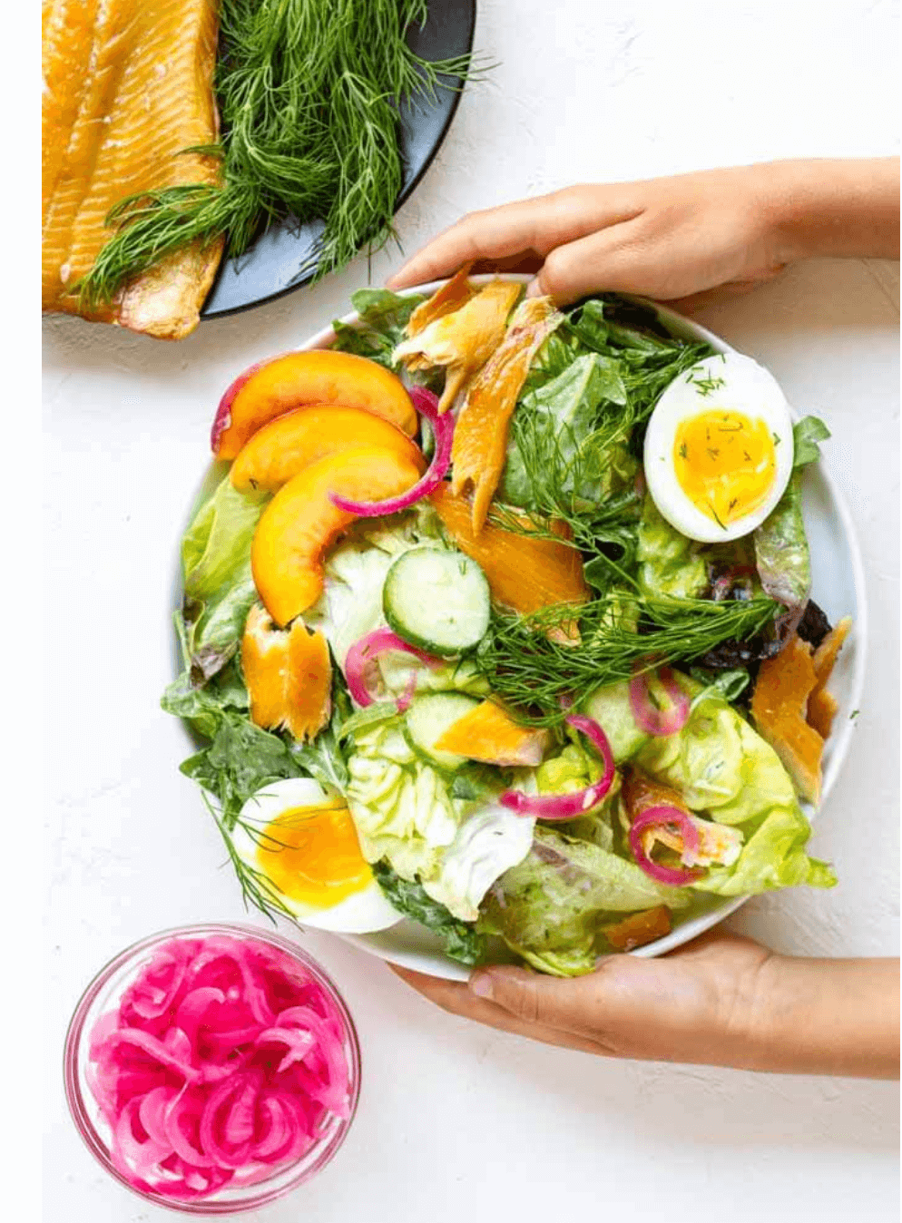 hands holding white plate with smoked trout salad